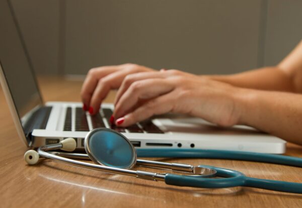 person sitting while using laptop computer and green stethoscope near